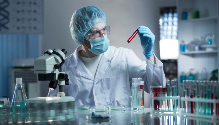 Doctor in a research lab holding up a red test tube with his left hand