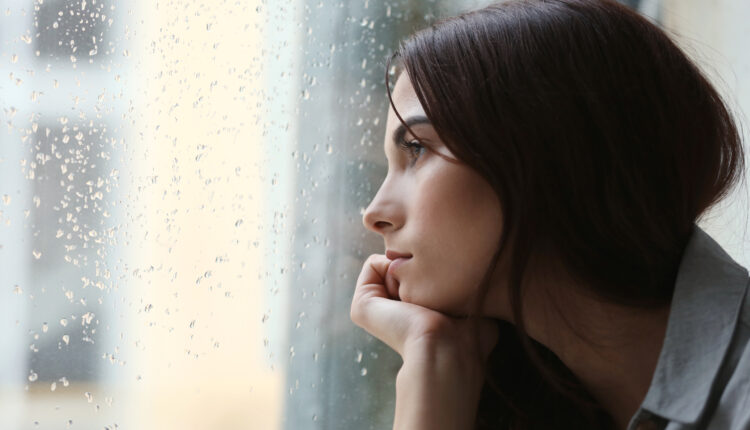 Depressed woman with dark brown hair looking out window. It's raining outside.